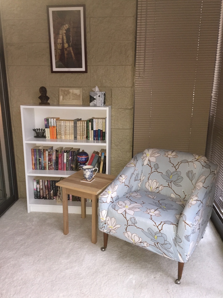 Photo of chair, side table with coffee mug, and short bookcase with books on each shelf.